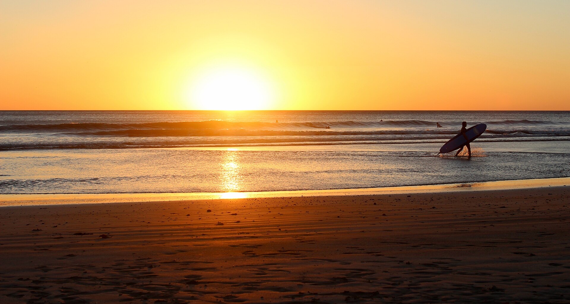 A surfer carrying a board at sunset on the beach at San Juan del Sur, Nicaragua